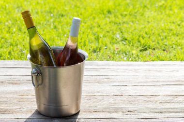 Açık bir bahçe masasında buz kovasında beyaz ve gül şarabı şişeleri harika bir yaz partisi sahnesi hazırlıyor. Kopyalama alanı ile