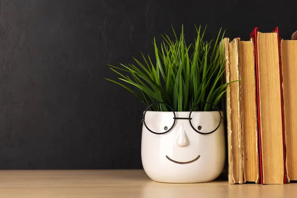 Old books on a table, potted plant with face and glasses and copy space for your text