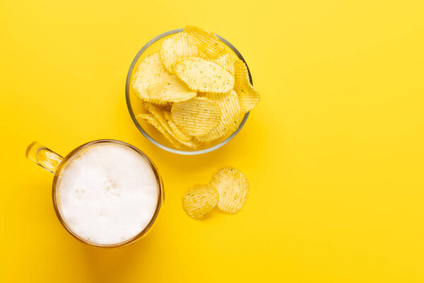 A tempting snack of beer and chips on a vibrant yellow background with copy space. Flat lay