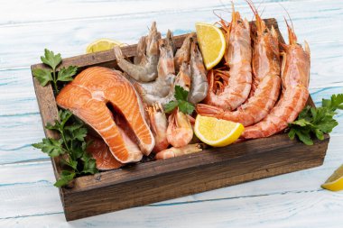 Karides, Langoustines ve ahşap kutuda alabalık bifteği gibi taze deniz ürünlerinin üst görüntüsü.