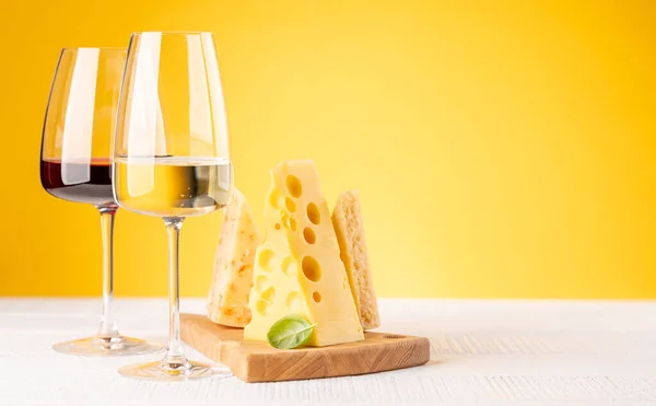 ボード上の様々なチーズ 赤と白のワイン 黄色の背景にコピースペース — ストック写真