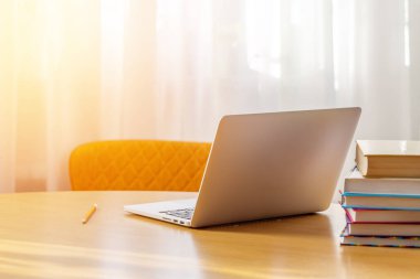 Laptop on a desk with stack of books and sunlight from window