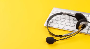 Sarı arkaplan üzerinde bir bilgisayar klavyesinde kulaklık ve metin için boş alan