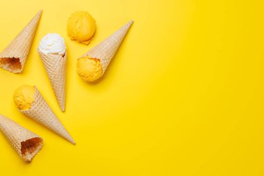 Lezzetli bir waffle külahında çeşitli dondurma aromaları, her tat tomurcuğu için bir ikram. Fotokopi alanı olan sarı arkaplan üzerinde düz uzanır