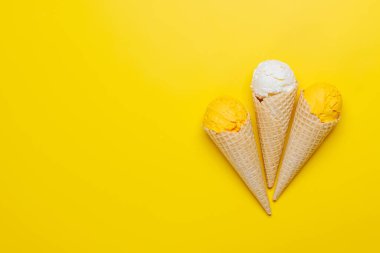 Lezzetli waffle külahlarında çeşitli dondurma aromaları, her tat tomurcuğu için bir ikram. Fotokopi alanı olan sarı arkaplan üzerinde düz uzanır
