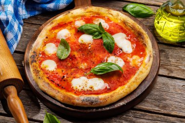 Ev yapımı margarita pizza, üzerine taze domates, mozzarella peyniri ve aromatik fesleğen yaprakları. Açık hava bahçe masasında.