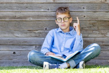 Çimen tarlasında kitap okuyan bir çocuk. Kopyalama alanı olan düz