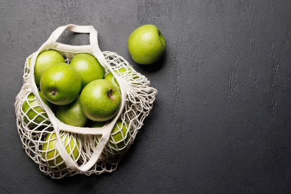 Mesh bag with fresh green apples on stone table. Flat lay with copy space