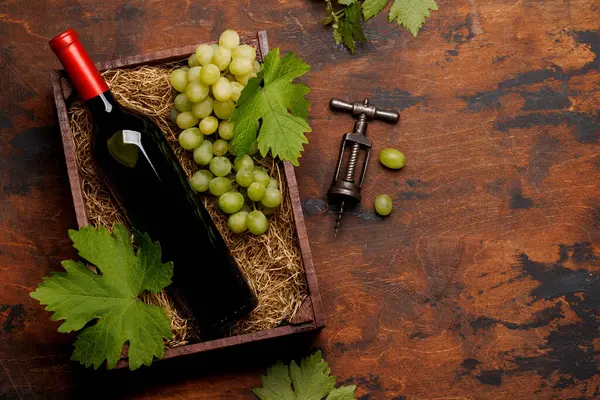 A red wine bottle and fresh grapes, presented in a rustic wooden box. Flat lay with copy space