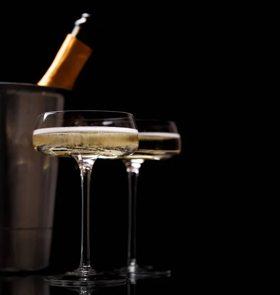 Two champagne glasses and champagne bottle in ice bucket on a black background with copy space