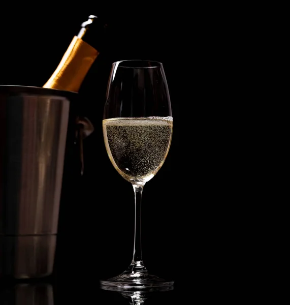 Champagne glass and champagne bottle in ice bucket on a black background with copy space