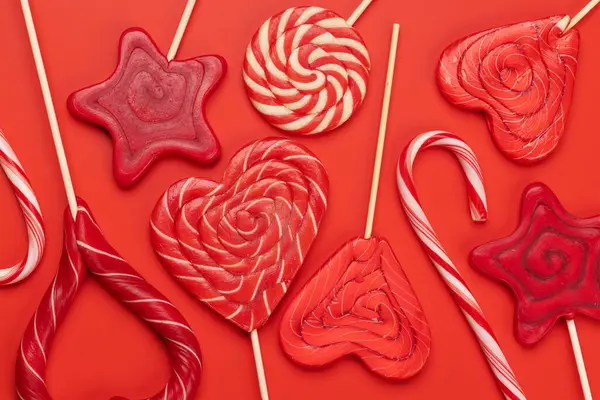 Various red candy sweets lollipops on red background. Valentines day candy hearts. Flat lay