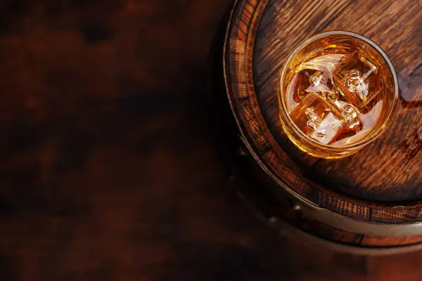 stock image Whiskey glass with ice on a rustic barrel, a classic sip. With copy space