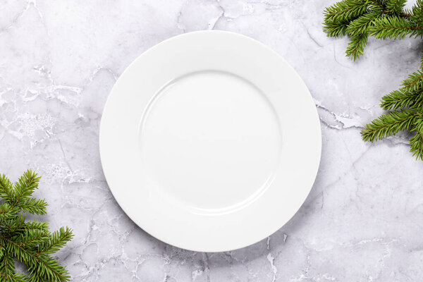 Mockup for a festive Christmas meal: Empty plate with festive fir tree branches. Flat lay with copy space