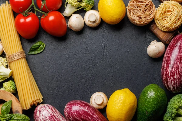 Frame of variety of vegetables and pasta. Flat lay over dark stone background with copy space