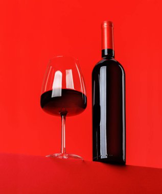 Kırmızı şarap zarafeti: canlı kırmızı arka plana karşı şarap kadehi ve şişe. Kopyalama alanı ile