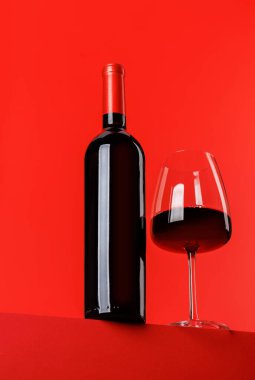 Kırmızı şarap zarafeti: canlı kırmızı arka plana karşı şarap kadehi ve şişe. Kopyalama alanı ile