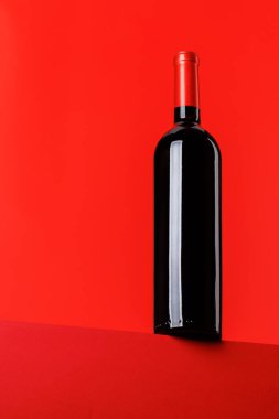 Kırmızı şarap zarafeti, canlı kırmızı arka plana karşı şarap şişesi. Kopyalama alanı ile