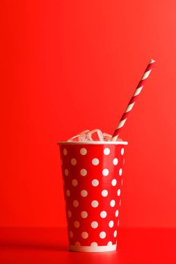 Kırmızı zemin üzerinde kola ve buz olan kağıt bardak, kopyalama alanı ile