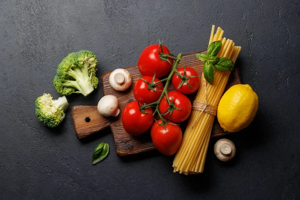 Variety of vegetables and pasta. Flat lay over dark stone background with copy space