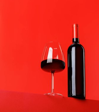 Kırmızı şarap zarafeti: canlı kırmızı arka plana karşı şarap kadehi ve şişe. Kopyalama alanı ile