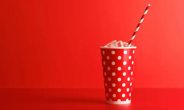 Paper cup with cola and ice over red background, with copy space