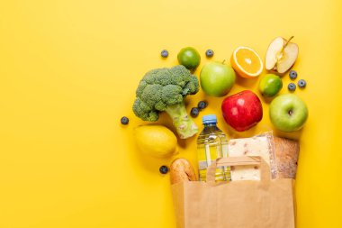 Sarı arka planda sağlıklı yiyeceklerle dolu bir alışveriş poşeti. Kopyalama alanı olan düz