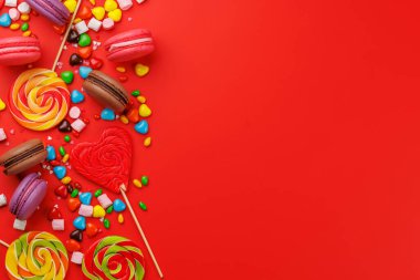 Çeşitli renkli şekerler, lolipoplar ve badem kurabiyeleri. Kopya alanı ile kırmızı arkaplan üzerinde düz yatıyordu