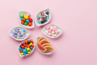 Çeşitli renkli şekerler, lolipoplar. Fotokopi alanı ile pembe arkaplan üzerinde düz yatıyordu