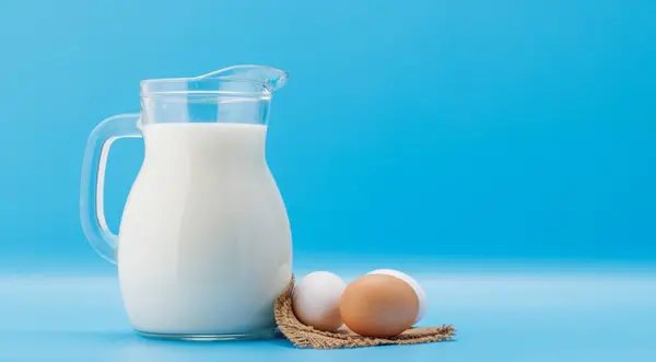 Krug Milch Mit Eiern Auf Blauem Hintergrund Mit Kopierraum lizenzfreie Stockfotos