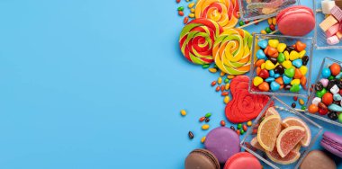 Çeşitli renkli şekerler, lolipoplar ve badem kurabiyeleri. Fotokopi alanı ile mavi arkaplan üzerinde tatlılar yatıyordu