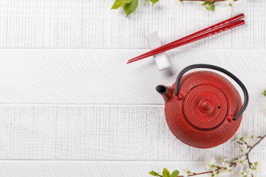 Japon yemek kültürünü simgeleyen kiraz çiçeği dalıyla süslenmiş çaydanlık ve yemek çubuklarıyla dolu bir masa.