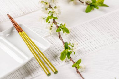 Boş tabak kiraz çiçeği dalı ve yemek çubuklarıyla süslenmiş, Japon yemek kültürünün somut bir örneği, geniş bir kopya alanı sağlıyor.
