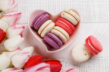 Pastel renkli laleler ve canlı kurabiyeler kalp şeklindeki bir kaseyi doldurur. Kutlamalar ve neşeli anlar için mükemmel ve büyüleyici bir sahne sunar.