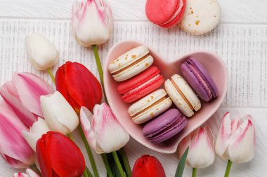 Pastel renkli laleler ve canlı kurabiyeler kalp şeklindeki bir kaseyi doldurur. Kutlamalar ve neşeli anlar için mükemmel ve büyüleyici bir sahne sunar.