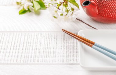 Boş tabak kiraz çiçeği dalı ve yemek çubuklarıyla süslenmiş, Japon yemek kültürünün somut bir örneği, geniş bir kopya alanı sağlıyor.