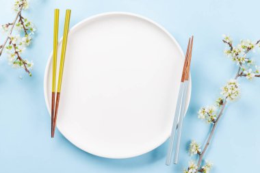 Boş tabak kiraz çiçeği dalı ve yemek çubuklarıyla süslenmiş, Japon yemek kültürünün somut bir örneği, geniş bir kopya alanı sağlıyor.