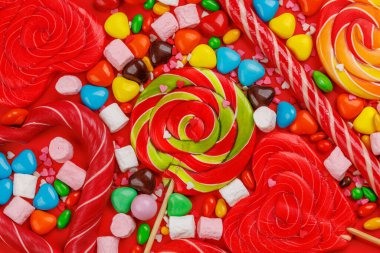 Çeşitli renkli şekerler, lolipoplar ve badem kurabiyeleri. Kırmızı arkaplan üzerinde düz yatıyordu
