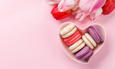 Pastel renkli laleler ve canlı kurabiyeler kalp şeklindeki bir kaseyi doldurur. Kutlamalar ve neşeli anlar için mükemmel ve büyüleyici bir sahne sunar.