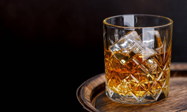 Whiskey glass with ice on a rustic barrel, a classic sip. With copy space