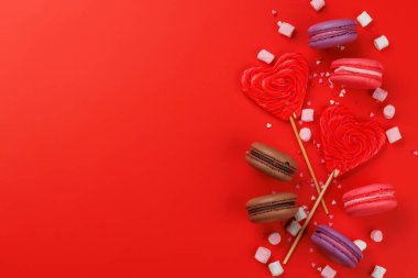 Çeşitli renkli şekerler, lolipoplar ve badem kurabiyeleri. Kopya alanı ile kırmızı arkaplan üzerinde düz yatıyordu