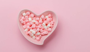 Kalp şeklindeki kasede rengarenk şekerlemeler. Aşk tatlıları pembe arkaplanda fotokopi alanı ile