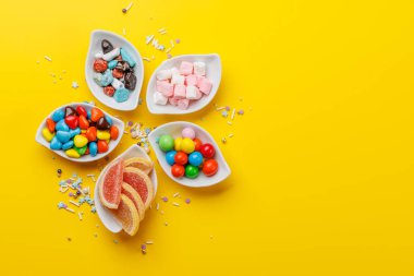 Çeşitli renkli şekerler, lolipoplar. Fotokopi alanı ile sarı arkaplan üzerinde düz yatıyordu