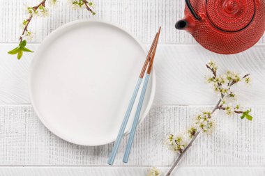 Boş tabak kiraz çiçeği dalı ve yemek çubuklarıyla süslenmiş, Japon yemek kültürünün somut bir örneği, geniş bir kopya alanı sağlıyor.