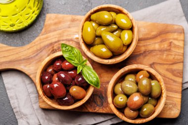 Bir kâse ve zeytin yağı şişesinde sunulan çeşitli zeytinlerin değişik renkleri, dokuları ve tatları sergilenmektedir.