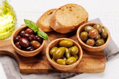 Bir kâse ve zeytin yağı şişesinde sunulan çeşitli zeytinlerin değişik renkleri, dokuları ve tatları sergilenmektedir.