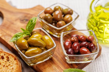 Bir kâse ve zeytin yağı şişesinde sunulan çeşitli zeytinlerin değişik renkleri, dokuları ve tatları sergilenmektedir.