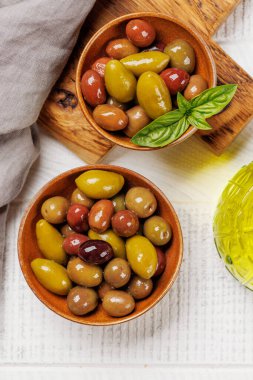 Bir kâse ve zeytin yağı şişesinde sunulan çeşitli zeytinlerin değişik renkleri, dokuları ve tatları sergilenmektedir.