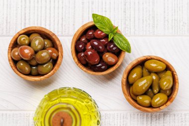 Bir kâse ve zeytin yağı şişesinde sunulan çeşitli zeytinlerin değişik renkleri, dokuları ve tatları sergilenmektedir.