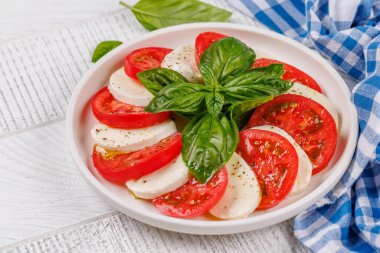 Canlı ve iştah açıcı bir Caprese antipasti. İçinde olgun domatesler, taze mozarella ve aromatik fesleğen yaprakları var.